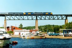 a train is going over a bridge with boats in the water and buildings on either side