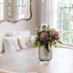 a vase filled with flowers sitting on top of a wooden table next to a mirror