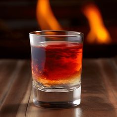 a glass filled with liquid sitting on top of a wooden table next to a fire place