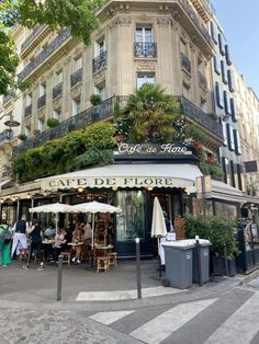 people sitting at tables in front of a cafe with plants growing on the building's roof