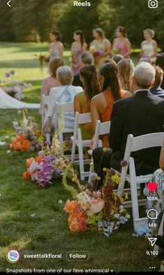 an outdoor ceremony with people sitting in chairs and flowers on the aisle, looking at each other