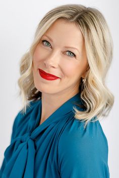 a woman with blonde hair wearing a blue shirt and red lipstick is smiling at the camera