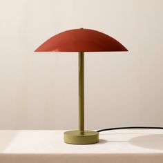 a red lamp sitting on top of a table next to a white wall and floor