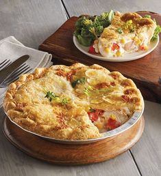 two pies sitting on top of a wooden cutting board next to a fork and knife