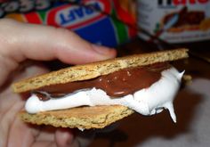 a person is holding up a chocolate covered biscuit with marshmallows on it