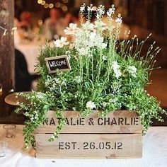 a wooden box filled with lots of flowers on top of a white table covered in greenery