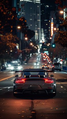 a white sports car driving down the street at night with city lights in the background