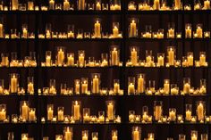 many lit candles are arranged in rows on shelves