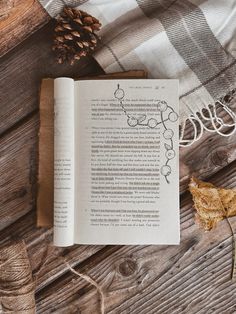 an open book sitting on top of a wooden table next to a pine cone and yarn