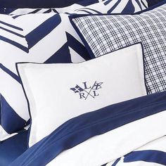 a bed with blue and white sheets, pillows and blankets on top of each other