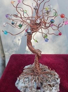 a wire tree sculpture with colorful glass beads on it's branches, sitting on a red velvet surface