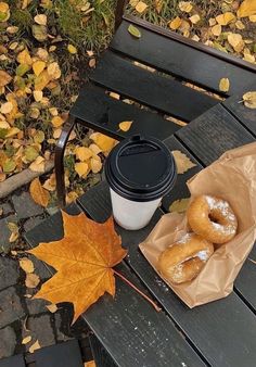 two doughnuts and a cup of coffee on a wooden bench in the fall