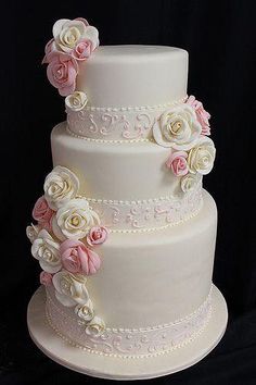 a three tiered wedding cake with pink and white flowers on the top, sitting on a black background