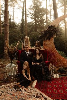 three people sitting on a red chair in the middle of an area with trees and rugs