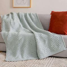 a couch with a blanket on top of it next to pillows and a framed picture