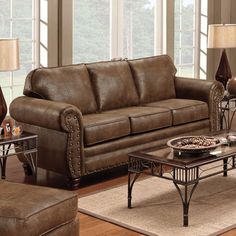 a living room with couches, tables and lamps in front of large windows that look out onto the woods