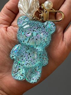 a hand holding a blue teddy bear keychain with a pearl bead on it