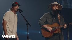 two men singing into microphones while one plays an acoustic guitar and the other sings