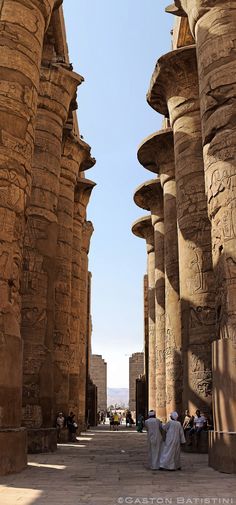 two men are sitting in front of some large stone pillars and looking up at the sky