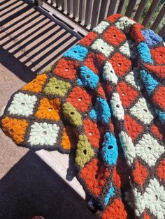 a crocheted blanket sitting on top of a wooden bench