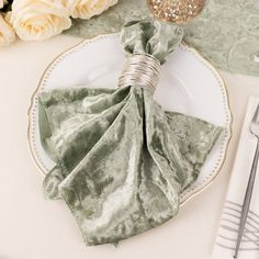 a white plate topped with green napkins next to silverware and flowers on top of a table