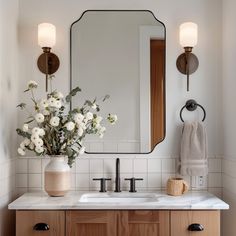 a bathroom vanity with flowers in a vase on the counter and a mirror above it