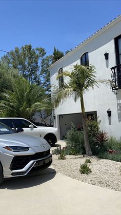 a silver sports car parked in front of a white house with palm trees on the driveway