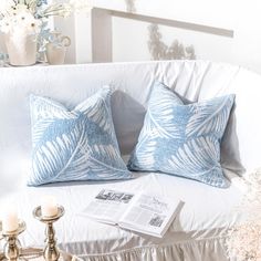 two blue pillows sitting on top of a white couch next to a vase with flowers