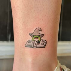 a small tattoo on the leg of a woman reading a book with a hat and eye patch