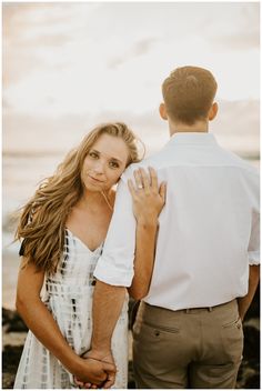 a man and woman standing next to each other in front of the ocean at sunset