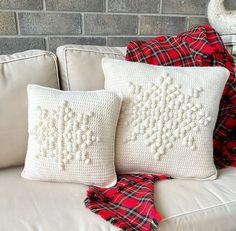 two white pillows sitting on top of a couch next to a red plaid throw pillow