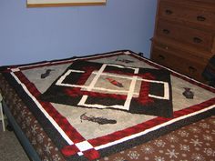 a bed with a red and black quilt on it in a bedroom next to a dresser