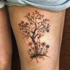 a woman's thigh with a tree and flowers tattoo on the side of her leg