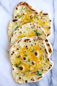 four flatbreads with cheese and herbs on a white marble countertop, ready to be eaten