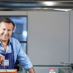 a smiling man in an apron stirring a bowl of food