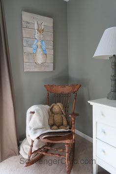 a teddy bear sitting in a wooden rocking chair next to a dresser and painting on the wall