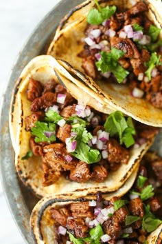 three tacos with meat, onions and cilantro on a gray plate next to a fork