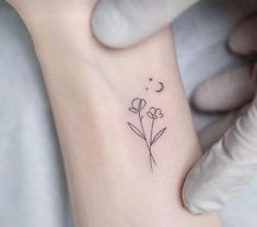 a small flower tattoo on the ankle is being held up by someone's hand