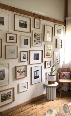 a living room filled with lots of framed pictures on the wall above a chair and table