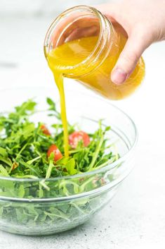 someone pouring dressing into a salad in a glass bowl on the counter top with tomatoes and lettuce