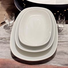 three white plates stacked on top of each other next to glasses and utensils