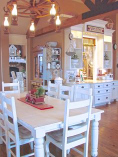 a dining room table with white chairs and lights on the ceiling above it, in front of an open kitchen area