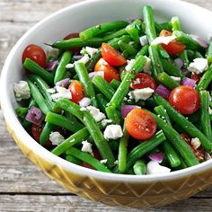 a bowl filled with green beans, cherry tomatoes and feta cheese on the side