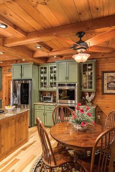 a large kitchen with green cabinets and wooden flooring on the walls, along with a dining table set for four