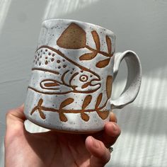 a hand holding a coffee mug with an image of a fish on the inside of it