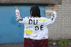 a woman wearing a white jacket with writing on it is standing in front of a blue door