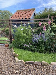 a garden with rocks and flowers in the foreground, next to a fenced off area