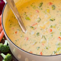 a bowl of broccoli cheese soup next to some carrots and other vegetables