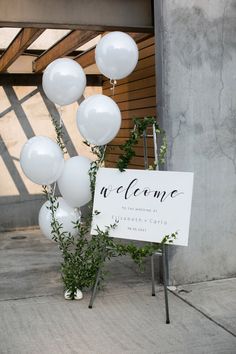 a welcome sign with white balloons attached to it