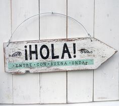 a wooden sign hanging from the side of a white building that says hola entre con - buuna onda